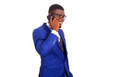 Yakışıklı genç bir işadamı beyaz arka planda izole bir şekilde duruyor ve gülümserken cep telefonuyla iletişim kuruyor.