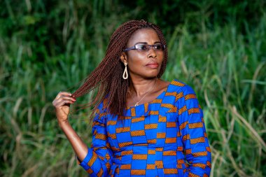 Yetişkin bir iş kadını gözlük takıyor, parkta saçlarıyla oynuyor ve yan bakıyor..