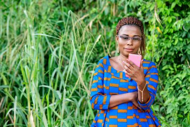 Geleneksel giysiler içinde güzel bir kadın parkta durup gülümserken cep telefonunu izliyor..