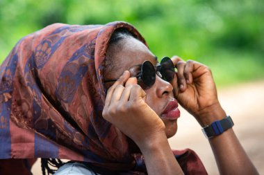 Güzel, yetişkin bir kadın, baş örtüsü takmış, güneş gözlüğü takıp doğayı seyrediyor..