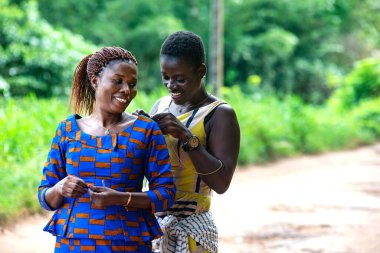 Güzel Afrikalı bir kadın kırsalda durup kız kardeşinin boynuna taktığı mücevheri takmasına yardım ediyor..