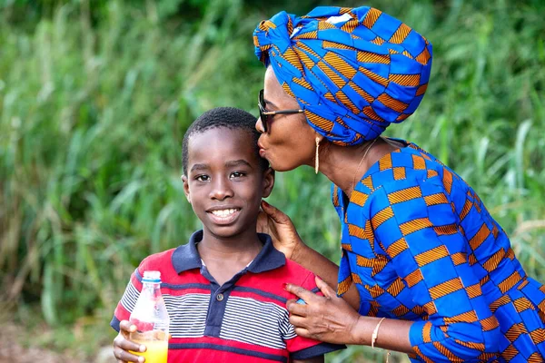 Geleneksel giysiler içinde güzel olgun bir kadın. Parkta durmuş, elinde meyve suyu şişesiyle, o gülümserken çocuğunu öpüyor..