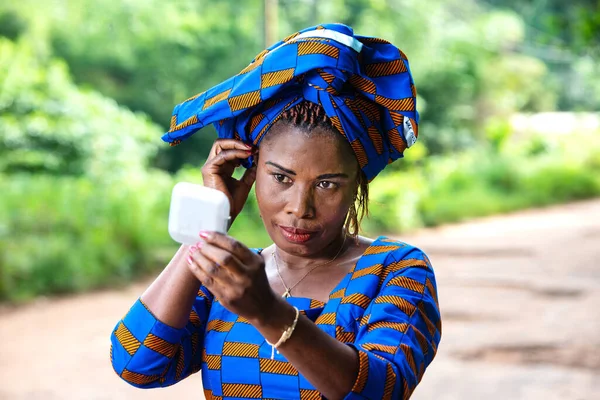 Beautiful adult business woman with a scarf and looking at her face in a small mirror on the street