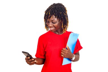 Arka planda duran kırmızı tişörtlü güzel bir kadın elinde bir belge tutucu ile cep telefonuna bakıp gülümsüyor.