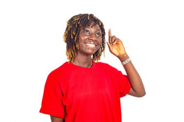 Kırmızı tişörtlü güzel bir kadın beyaz arka planda durup gülümserken parmağıyla işaret ediyor..