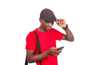 Kırmızı tişörtlü yakışıklı bir adam ve beyaz arka planda duran Kepi cep telefonuna bakıp gülümsüyor..