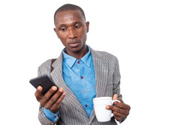 Yakışıklı, yetişkin bir işadamı elinde bir fincan kahve tutarken cep telefonu kullanıyor..