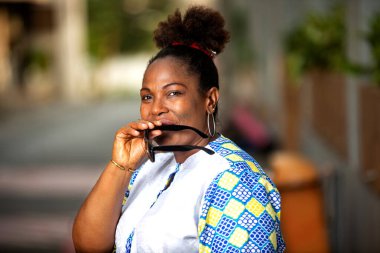 beautiful business woman standing on the street with sunglasses in hand, smiling at camera.