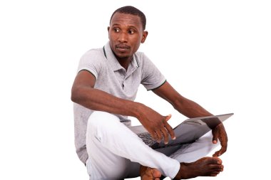 Genç adam dizüstü bilgisayar tutuyor yerde oturuyor ve yan bakıyor..