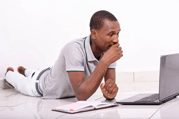 a handsome student in a t-shirt lying on the floor isolated on a white background is looking at laptop while thinking.
