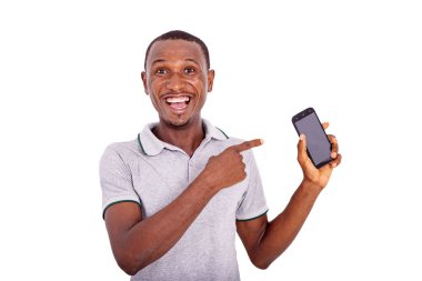 Yakışıklı, mutlu bir genç adam içeride durmuş cep telefonunu işaret ediyor ve kameraya gülümsüyor..