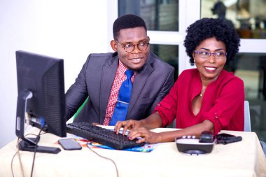 İş adamı ve gözlüklü bir kadın ofiste birlikte çalışırken gülümsüyor..