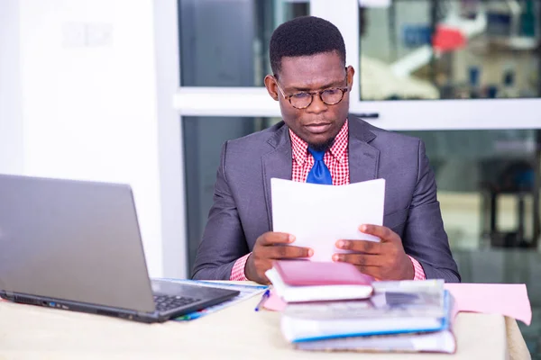 concentrated adult businessman sitting in front of laptop and reading report on paper in office.