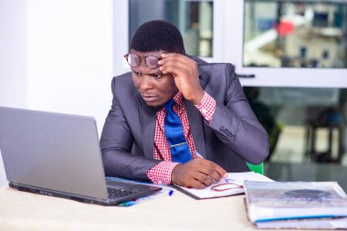 Ceketli yakışıklı iş adamı, masa başında dizüstü bilgisayar ve defter kullanarak çalışıyor..