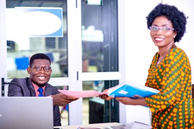 Çekmecede oturan yakışıklı bir işadamı meslektaşına bir dosya veriyor ve kameraya bakıp gülümsüyor..