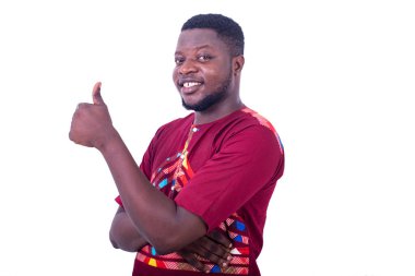 Beyaz arka planda duran peştemalli yakışıklı bir adam başparmağıyla gülümsüyor..