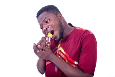 Beyaz arka planda duran peştemalli yakışıklı bir adam dişlerini kullanarak küçük bir şişe likör açıyor..