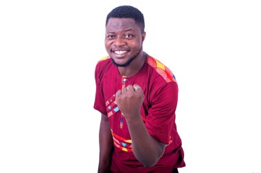 Geleneksel gömlek giyen yakışıklı genç adam zafer jesti yapıyor ve kollarını kaldırarak gülümsüyor..