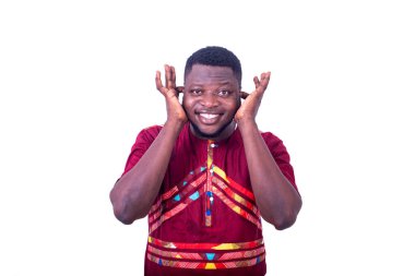 Beyaz arka planda duran peştemalli yakışıklı genç adam parmaklarını kullanarak kulaklarını kapatıyor ve gülümseyen kameraya bakıyor..