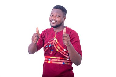 Beyaz arka planda duran peştemalli yakışıklı genç adam başparmağını kaldırıyor ve gülümsüyor..