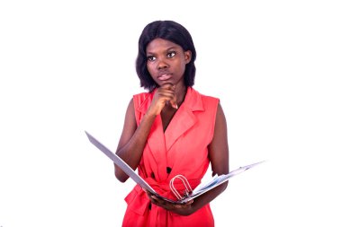 Beyaz bir arka planda duran ceketli genç ve güzel bir iş kadını. Elinde bir dosya dolabı var. Eli çenesinin altında ve uzaklığa bakıyor.