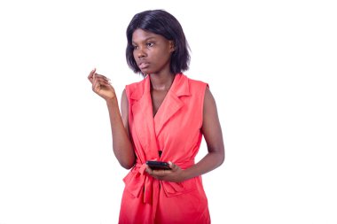 Ceketli genç ve güzel bir iş kadını elinde cep telefonuyla beyaz arka planda duruyor.