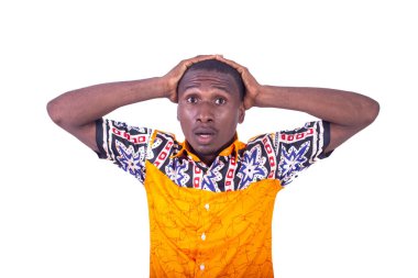 Beyaz arka planda duran, elleri başının üstünde duran, tişörtlü yakışıklı genç bir işadamı şaşırmış görünüyor.