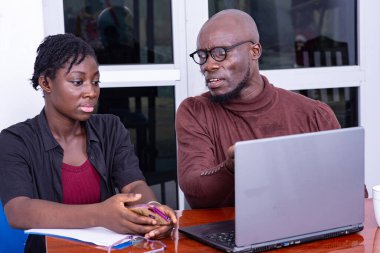 İş adamı ve kadın toplantı odasında dizüstü bilgisayarla oturmuş projeyi tartışıyorlar. Adam eliyle bir şey gösteriyor..