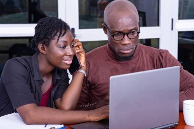 İki ciddi iş ortağı masada oturuyor ve dizüstü bilgisayarda birlikte çalışıyorlar. Kadın cep telefonuyla konuşuyor..