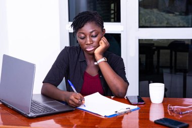 Genç iş kadını masada oturuyor ve dizüstü bilgisayarla çalışıyor.