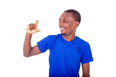 Beyaz arka planda duran mavi tişörtlü genç bir adam küçük bir jest yapıyor ve kameraya gülümsüyor..