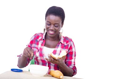 Masada oturan genç ve güzel bir kadın, kahvaltıdan zevk almak için ekmeğin üzerine tereyağı sürüyor..