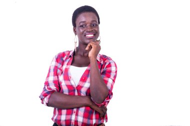 Dişli gömlekli genç bir kadın beyaz arka planda duruyor, çenesinin altında elleri kameraya bakıp gülümsüyor.