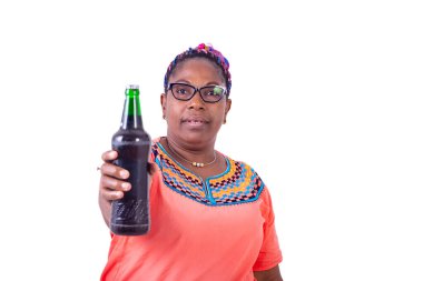 Beyaz arka planda duran gözlüklü Afrikalı bir kadın bir şişe bira veriyor..