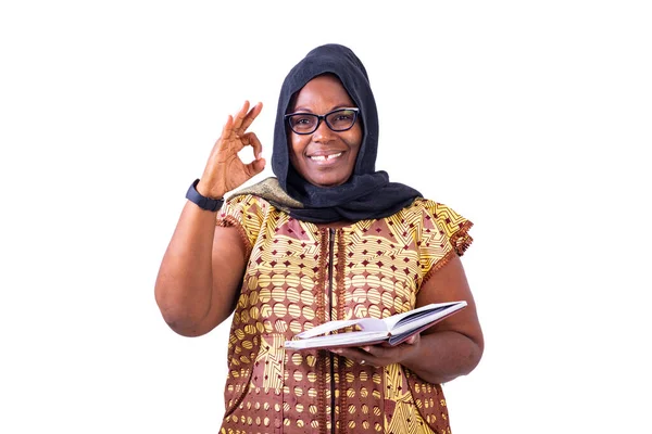 穆斯林成熟的女商人戴着眼镜 拿着笔记本 用手指做出正确的手势 同时对着相机微笑 — 图库照片