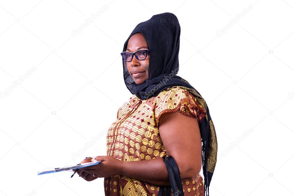 Muslim mature woman wearing glasses, standing sideways holding a clipboard.