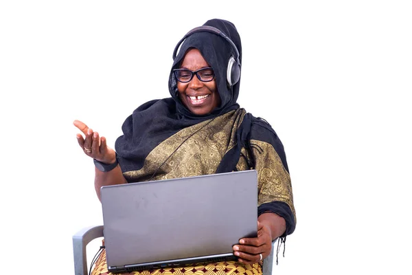 漂亮的穆斯林女商人坐在白色背景上 一边笑一边用笔记本电脑和耳机 — 图库照片