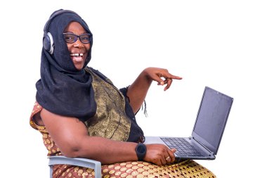 Güzel Müslüman iş kadını beyaz arka planda oturuyor, kulaklığı bilgisayara doğrultulmuş ve kameraya bakıp gülüyor..