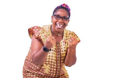 Olgun bir kadın ayakta durup kameraya gülümseyen kollarıyla zafer jesti yapıyor..