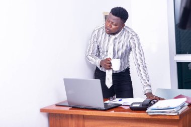 Genç, ciddi bir iş adamı masanın başında elinde bir fincan kahve tutuyor..