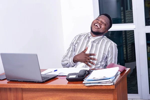 Excited adult businessman sitting at desk and laughing out loud and holding hand on stomach.