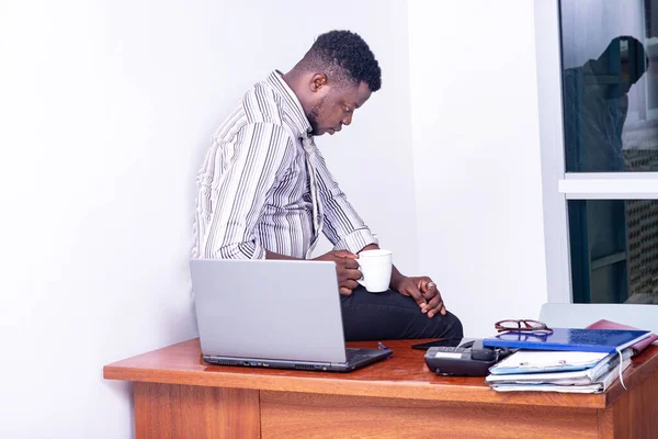 Młody Zestresowany Biznesmen Siedzi Stole Biurowym Trzymając Filiżankę Kawy — Zdjęcie stockowe