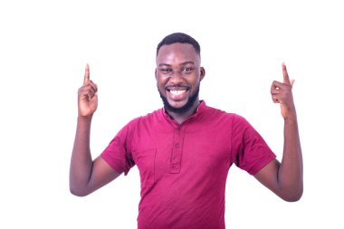 Kırmızı tişörtlü genç bir adam beyaz arka planda dikiliyor parmaklarını kaldırıp kameraya bakıyor ve gülüyor..