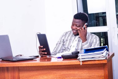 Genç işadamı kulaklık takıyor ve ofiste dijital tabletle ilgili bir video görüşmesi yapıyor..