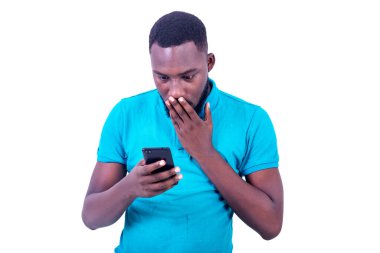 Yakışıklı, şaşırmış genç bir adam eliyle ağzını kapatıyor ve cep telefonunun ekranına bakıyor..