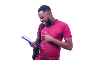 Beyaz bir arka planda duran ve sırt çantası takan genç bir öğrenci gülümserken bir kitabı gösterecek..