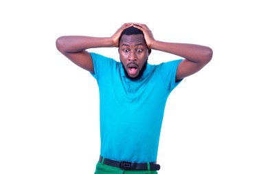 Şok olmuş genç bir adam ağzı açık, mavi tişört giyiyor, ellerini kafasında tutuyor..