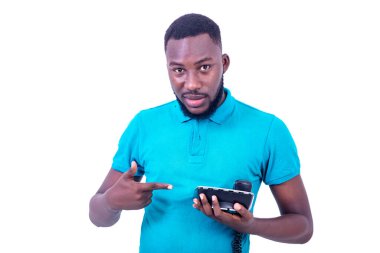 Beyaz arka planda duran mavi tişörtlü genç işadamı parmağıyla telefona gülümsüyor..