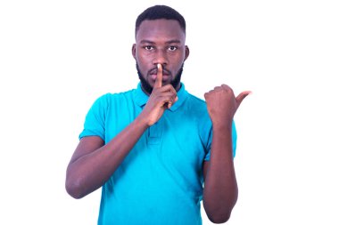 Mavi tişörtlü genç adam sakin olmak istiyor. Parmakları dudaklarında, parmakları yanda..