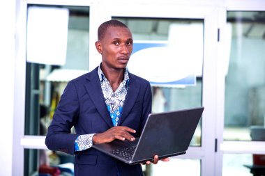 Genç, ciddi bir iş adamı, kameraya bakarken dizüstü bilgisayarla çalışıyor..